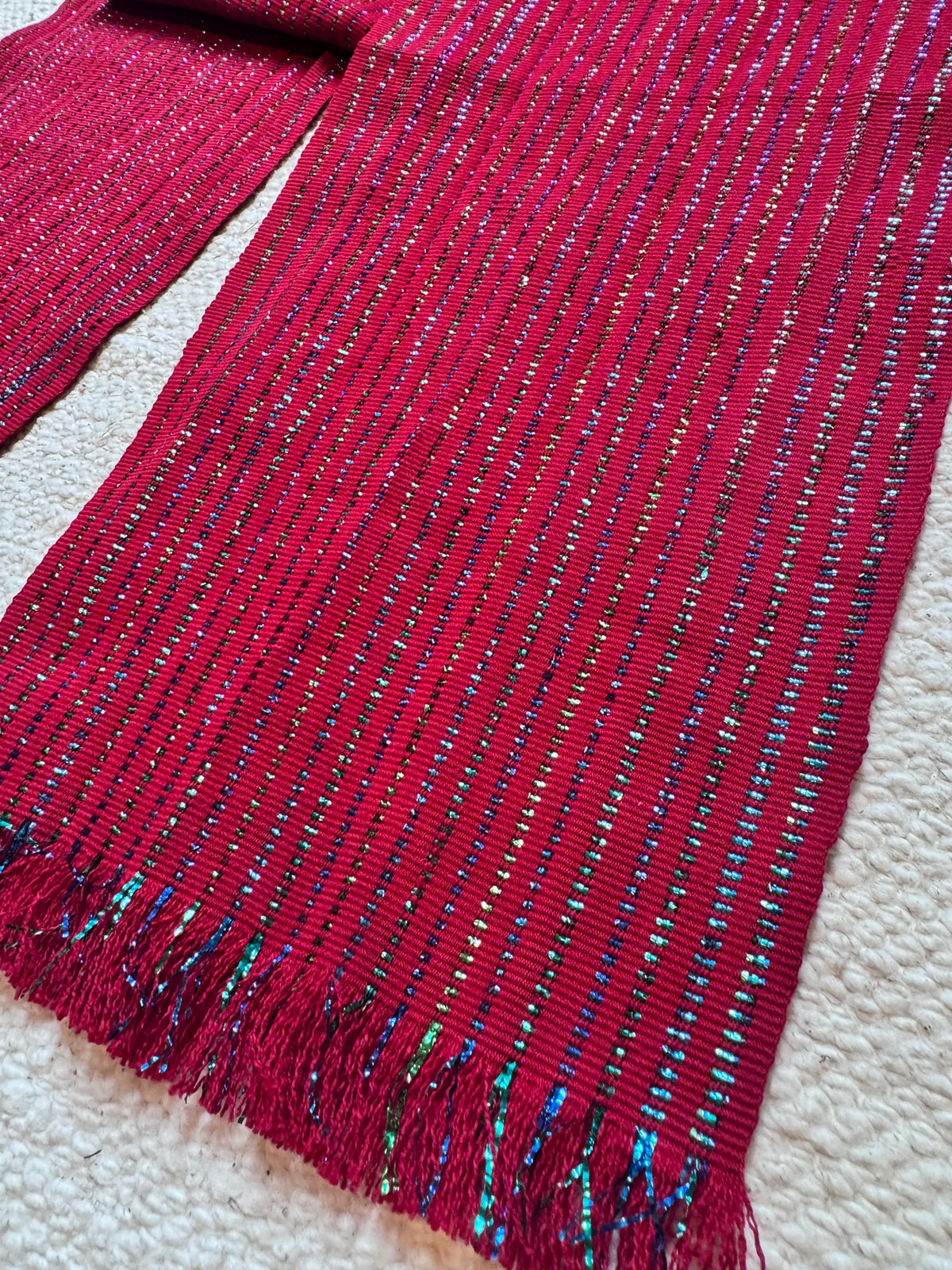Cherry-red Tocoyal hair wrap folded on a light background, showing metallic woven stripes and fringed ends. Vida Maya