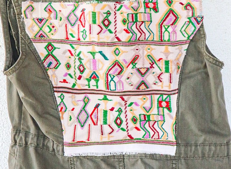 Angled back view of an olive-green vest showing its repurposed vintage Nebaj huipil panel