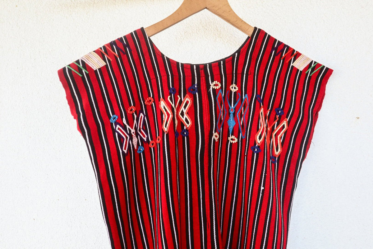 Close-up of colorful butterfly motifs and handwoven red, black, and white stripes on a vintage Chajul huipil