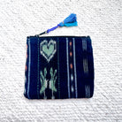 A small woven zip pouch with a dark navy blue base and light blue, white, and mint green geometric patterns, featuring a blue tassel zipper pull, laid flat on a white textured background.