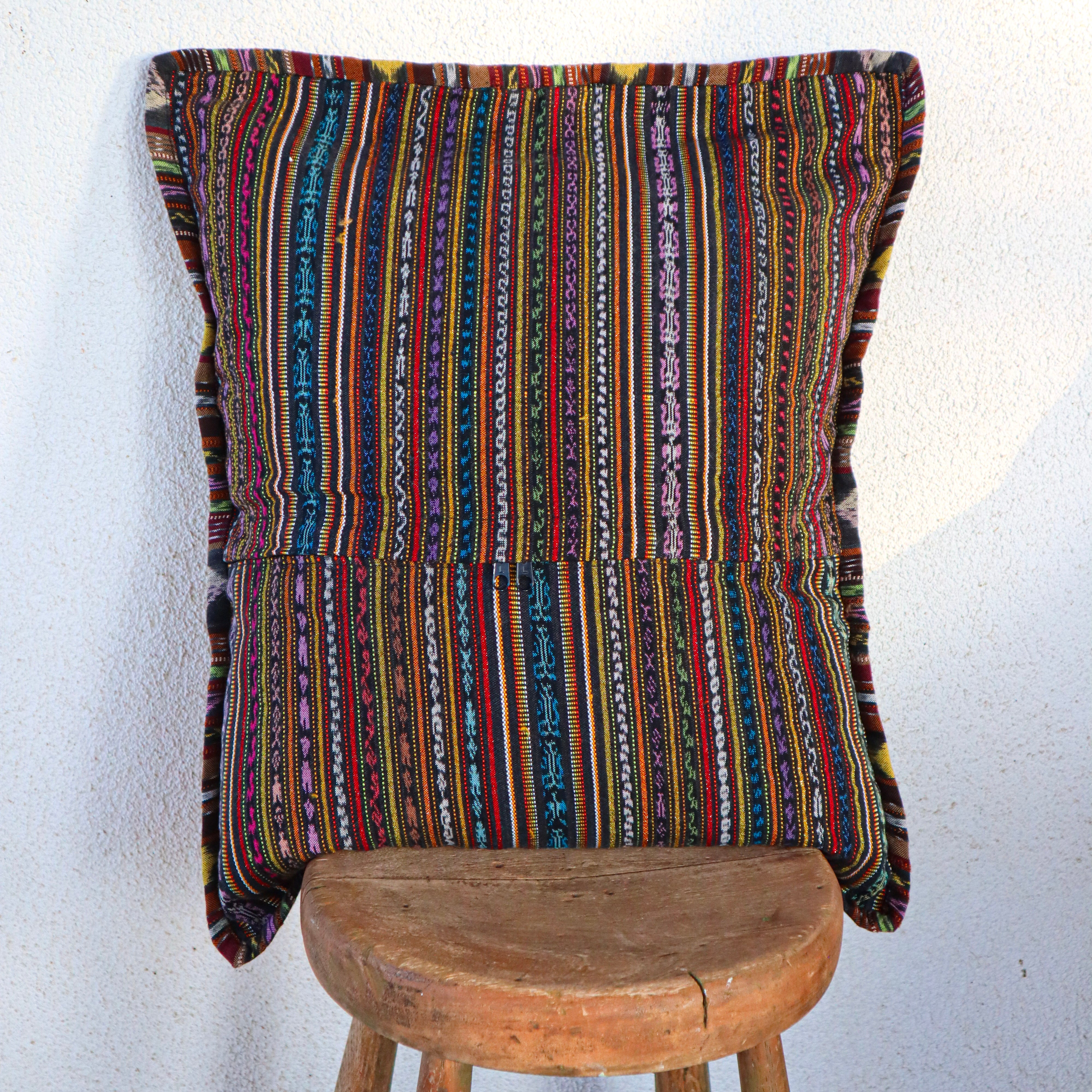 Multicolored striped pillow on a wooden stool against a white wall