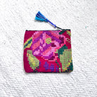 A small rectangular woven pouch with a colorful floral pattern in pink, purple, green, and red, featuring a blue tassel zipper pull, laid flat on a textured white surface.