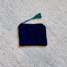 A small dark navy fabric pouch with a blue stripe detail and a teal tassel, placed on a textured off-white carpet.
