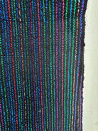 A close-up of a black woven textile with vertical multicolored stripes in blue, green, pink, and purple, next to a plain white background.