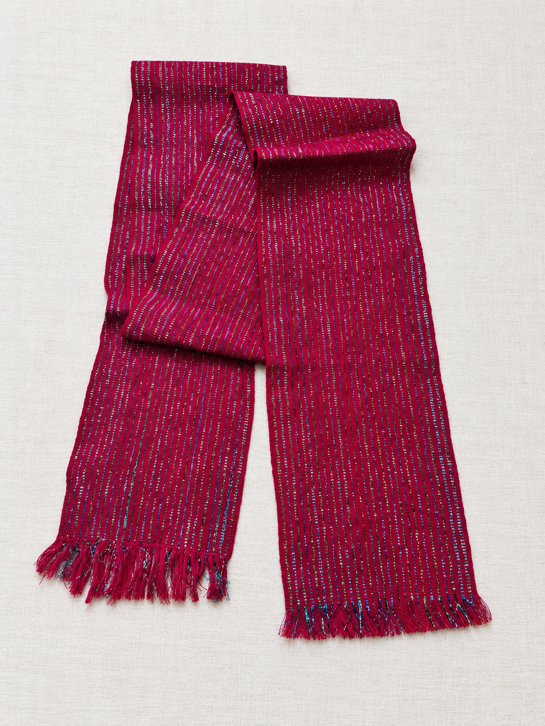 Cherry-red Tocoyal hair wrap folded on a light background, showing metallic woven stripes and fringed ends