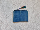 A small woven blue pouch or coin purse with a colorful tassel, placed on a textured off-white carpet.