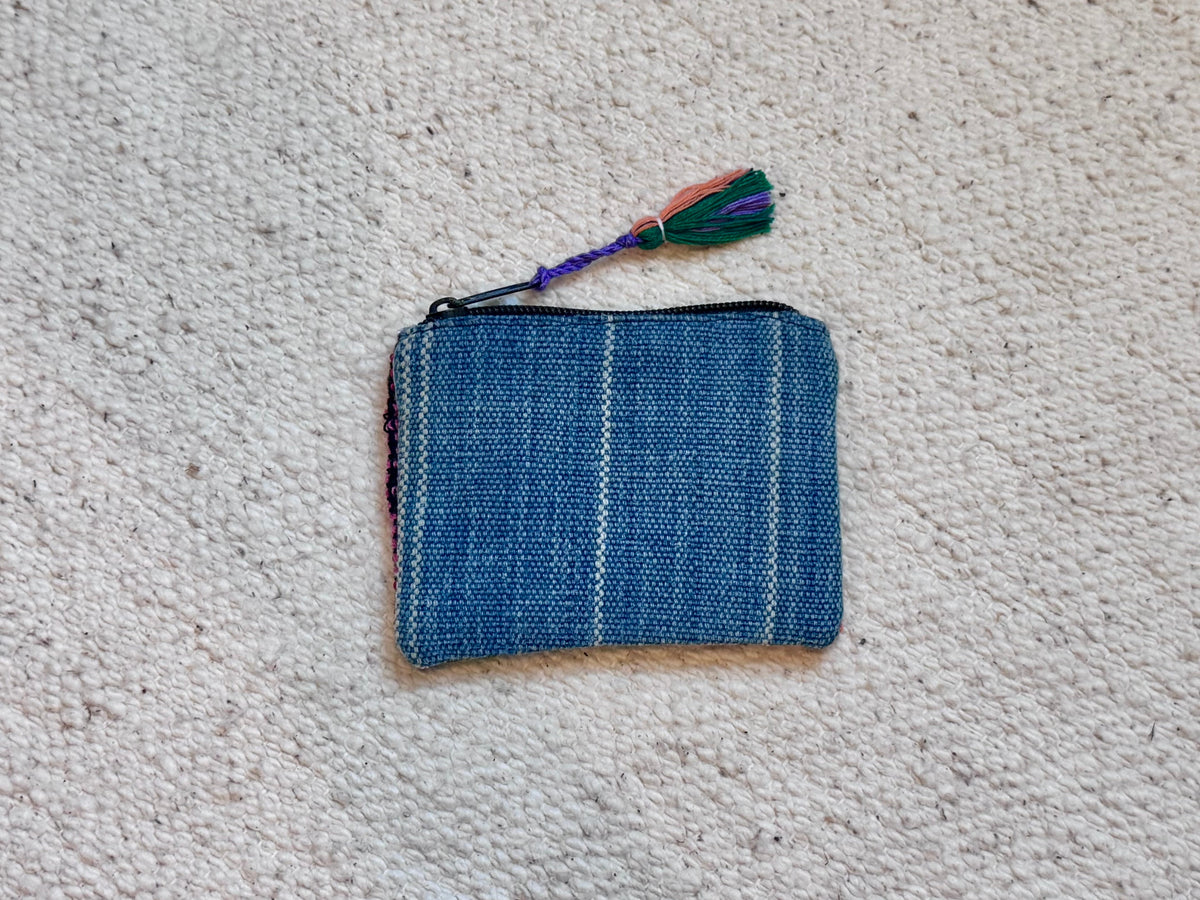 A small woven blue pouch or coin purse with a colorful tassel, placed on a textured off-white carpet.