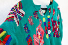 A vintage Mayan Huipil top with embroidered peacock and butterfly designs on a dark teal background, displayed on a wooden hanger.