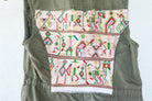 Angled back view of an olive-green vest showing its repurposed vintage Nebaj huipil panel