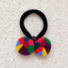 Soft Rainbow Chajul Tocoyal pom-pom hair tie with coral, pink, teal, yellow, green, lavender, and brown textile poms on a black band