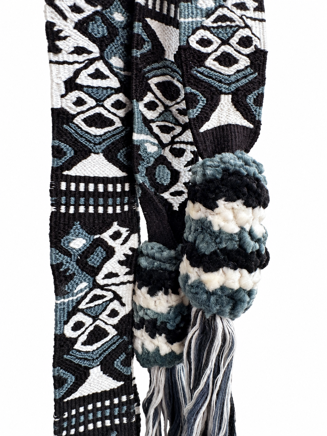 A close-up of a woven scarf with a geometric pattern in black, white, and blue, featuring a knitted cuff and tassel.