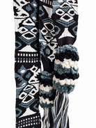 A close-up of a woven scarf with a geometric pattern in black, white, and blue, featuring a knitted cuff and tassel.