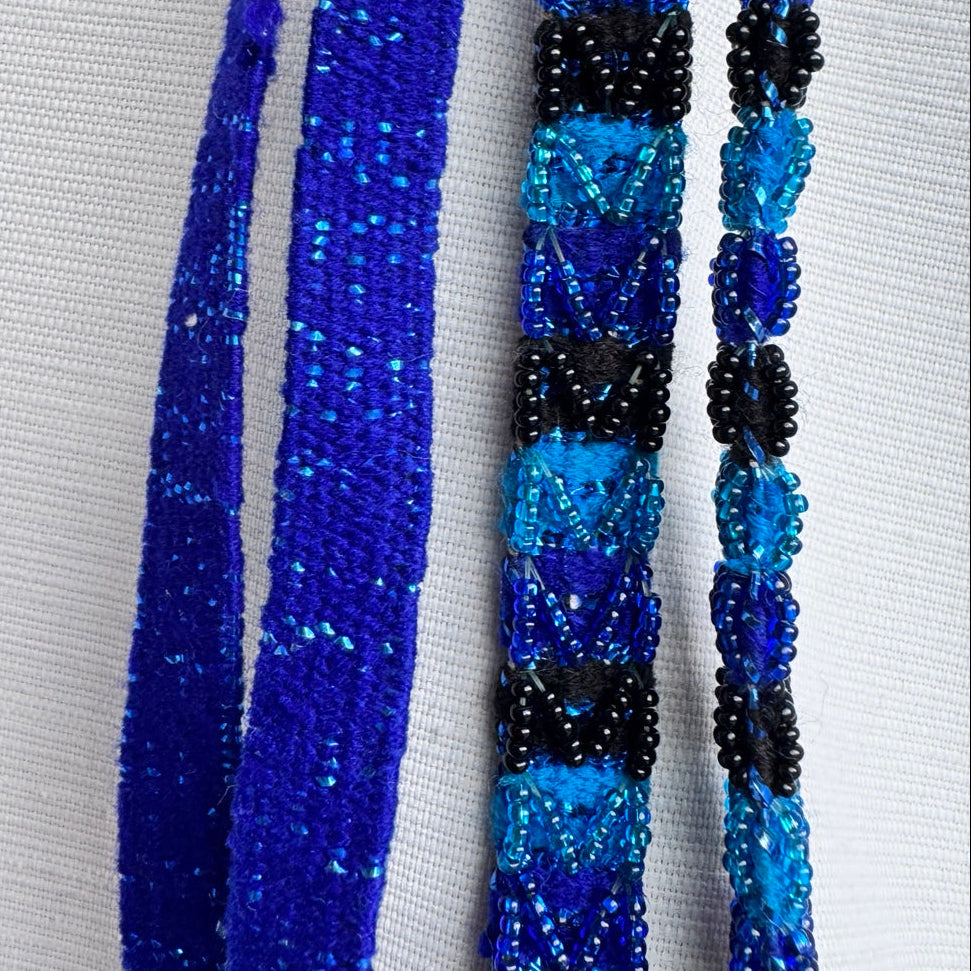 Three beaded necklaces displayed vertically against a white textured fabric background. The left necklace is a solid royal blue.
