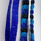 Three beaded necklaces displayed vertically against a white textured fabric background. The left necklace is a solid royal blue.