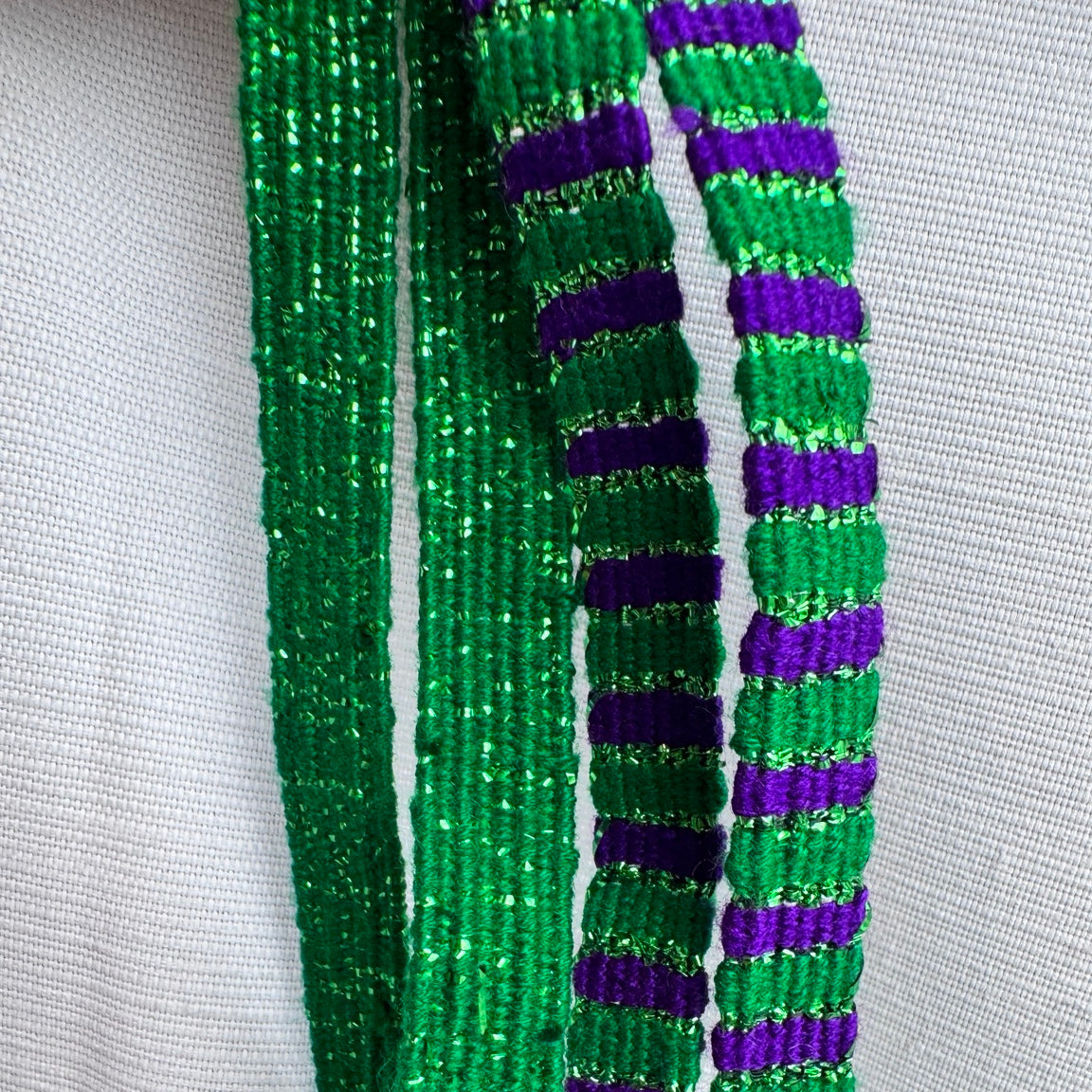 Three strands of beaded fringe with green and purple glitter beads, displayed against a white textured fabric background.