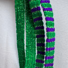 Three strands of beaded fringe with green and purple glitter beads, displayed against a white textured fabric background.