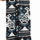 A close-up of a woven textile strap or belt with a geometric tribal pattern in black, white, and light blue, held by a hand on the left side against a white background.