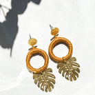A pair of gold-colored, round-shaped earrings with a textured surface, displayed against a shadowed background.