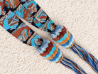 A pair of colorful woven rope accessories with striped knotted loops and patterned hanging strands, laid flat on a textured cream carpet.