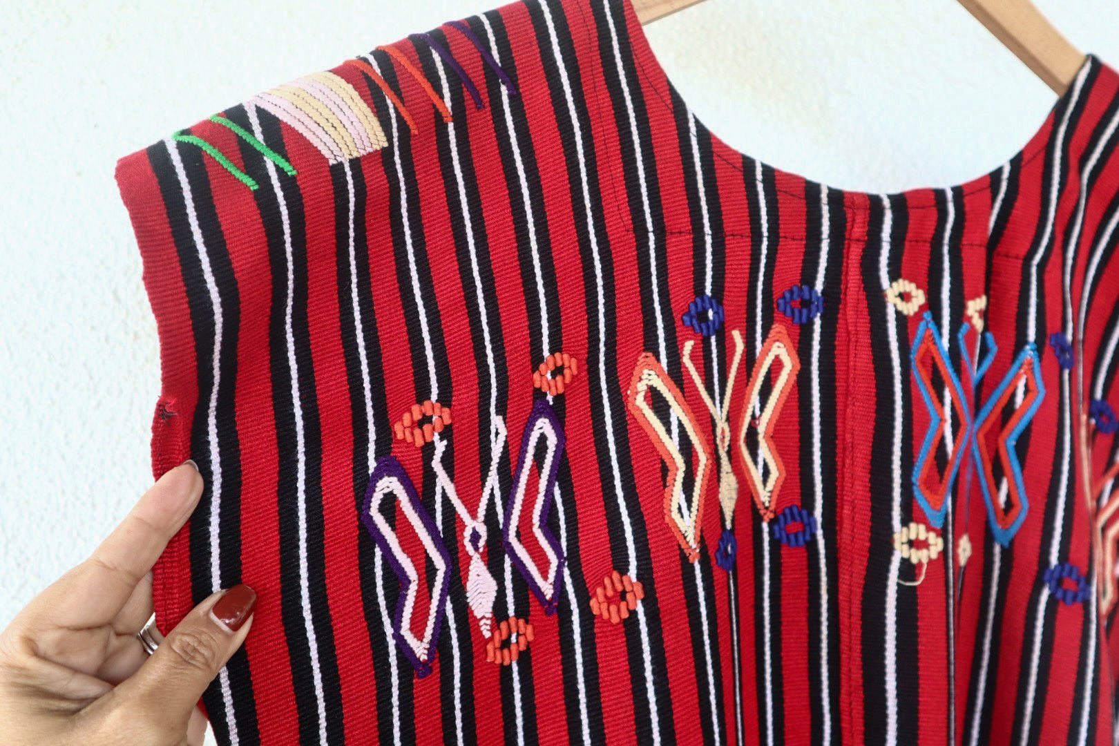Close-up of colorful butterfly motifs and handwoven red, black, and white stripes on a vintage Chajul huipil