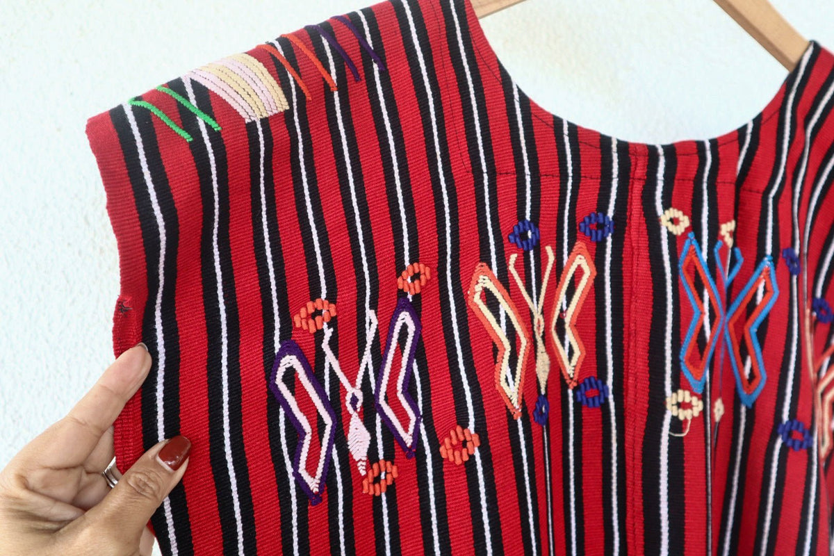 Close-up of colorful butterfly motifs and handwoven red, black, and white stripes on a vintage Chajul huipil