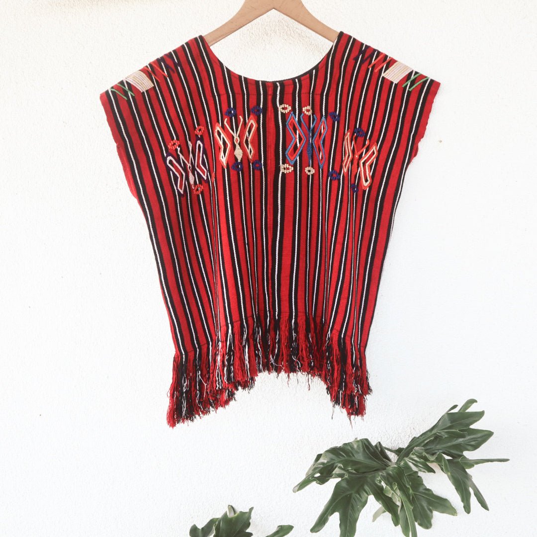 Close-up of colorful butterfly motifs and handwoven red, black, and white stripes on a vintage Chajul huipil