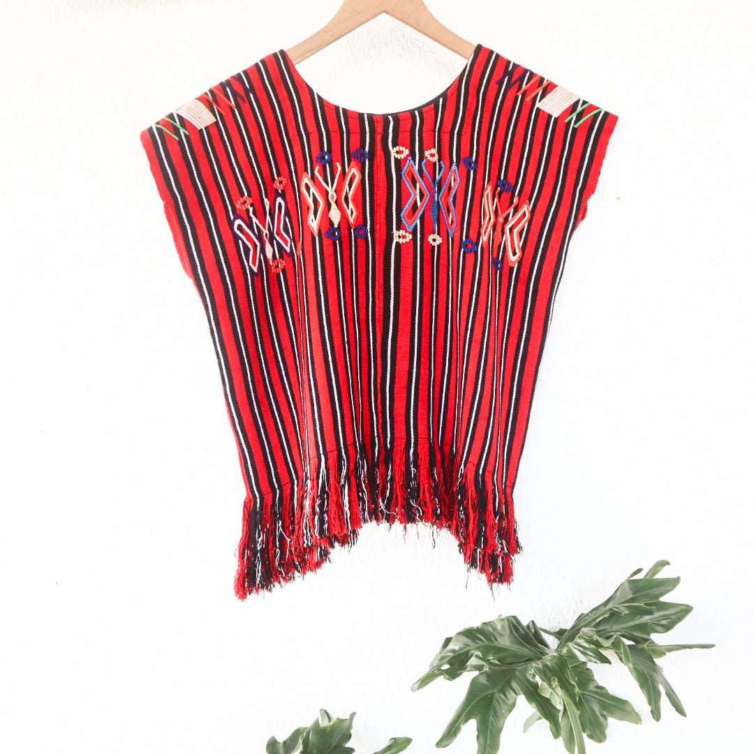 Close-up of colorful butterfly motifs and handwoven red, black, and white stripes on a vintage Chajul huipil